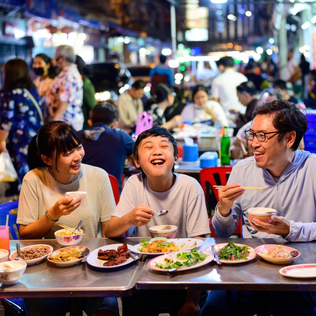 Asian family enjoy eating food on street food restaurant with crowd of people at Yaowarat road, Bangkok.